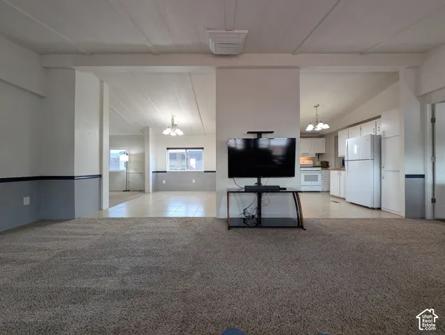 Open-concept living space featuring carpeted and tile flooring, white appliances, and a built-in kitchen