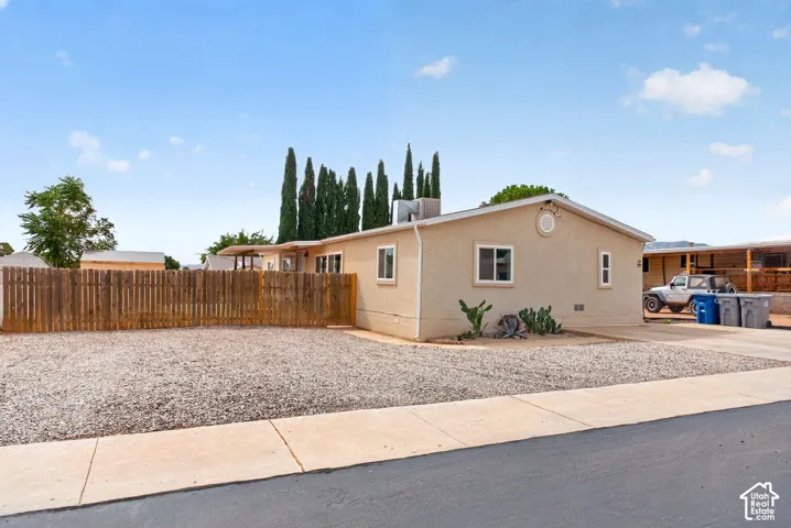 Stucco exterior featuring a gravel-surfaced lot, wood picket perimeter fencing, and an attached concrete driveway