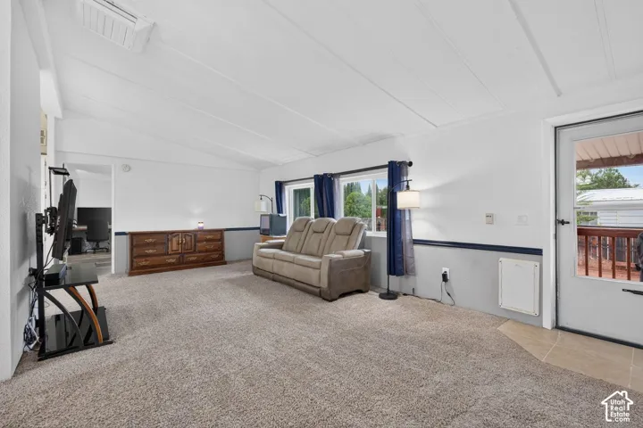 Living area featuring a vaulted ceiling, neutral wall-to-wall carpeting, dual-tone wall paint, and a door providing exterior access