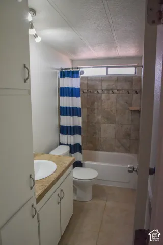 Main Bathroom featuring a single basin vanity with a laminate countertop, white cabinetry, tile flooring, a bathtub with a tiled shower surround, and an upper window