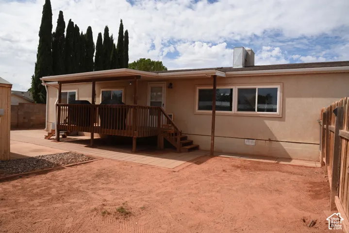 Front door exterior featuring a covered wood deck, flat roofline, stucco siding, and a wood fence