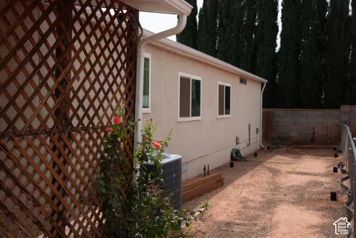 Stucco exterior with multiple windows, air conditioning unit, wood lattice privacy screen, and a block wall perimeter