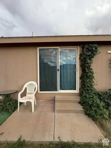 Sliding glass door access, concrete patio, two-step concrete entry, exterior wall siding, and established climbing greenery