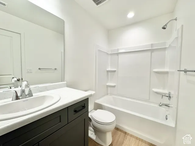 Bathroom featuring a tub/shower combination with white surround, a dark wood-finish vanity with white countertop, and wood-finish flooring