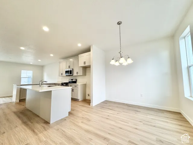 Modern open-concept kitchen and dining area featuring white cabinetry, stainless steel appliances, a large waterfall-edge island with seating, wood-finish flooring throughout, recessed ceiling lighting, and pendant fixtures suspended above the dining spac