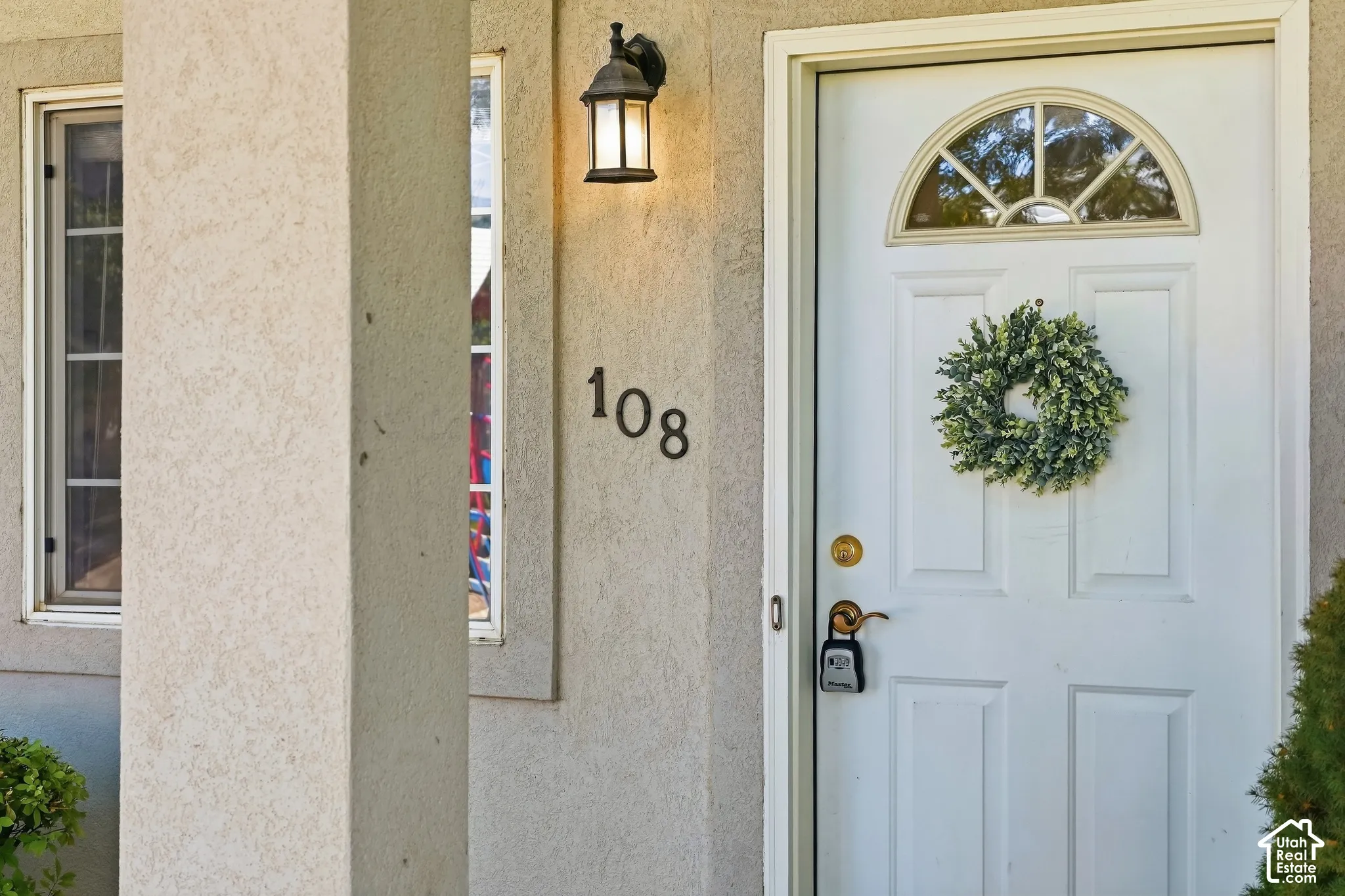 Front entry featuring a white door with an arched transom window, a wall-mounted exterior light fixture, and textured stucco siding