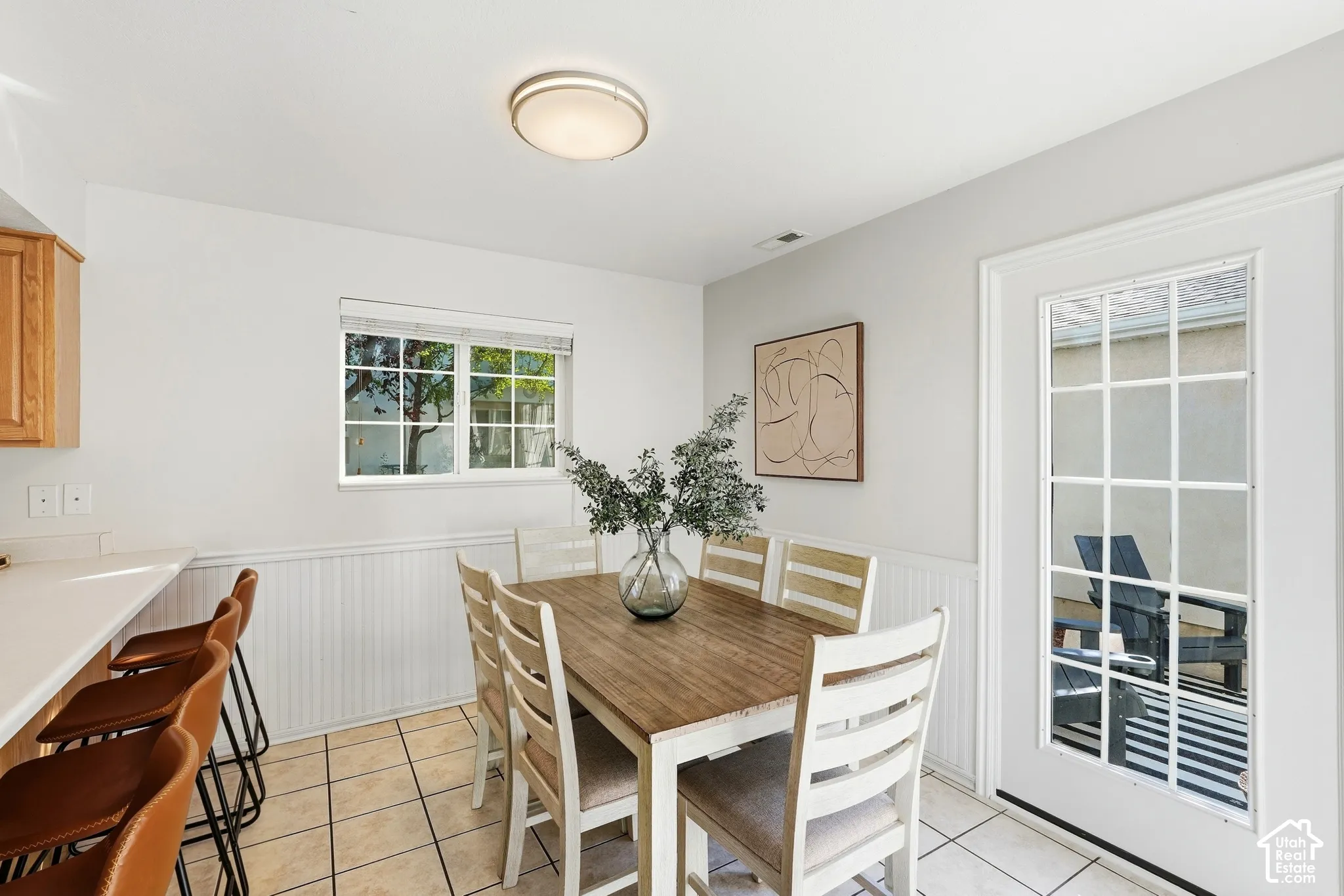 Dining area featuring tiled flooring, a built-in breakfast bar, a window with exterior views, white wainscoting, and a glass-paned exterior door