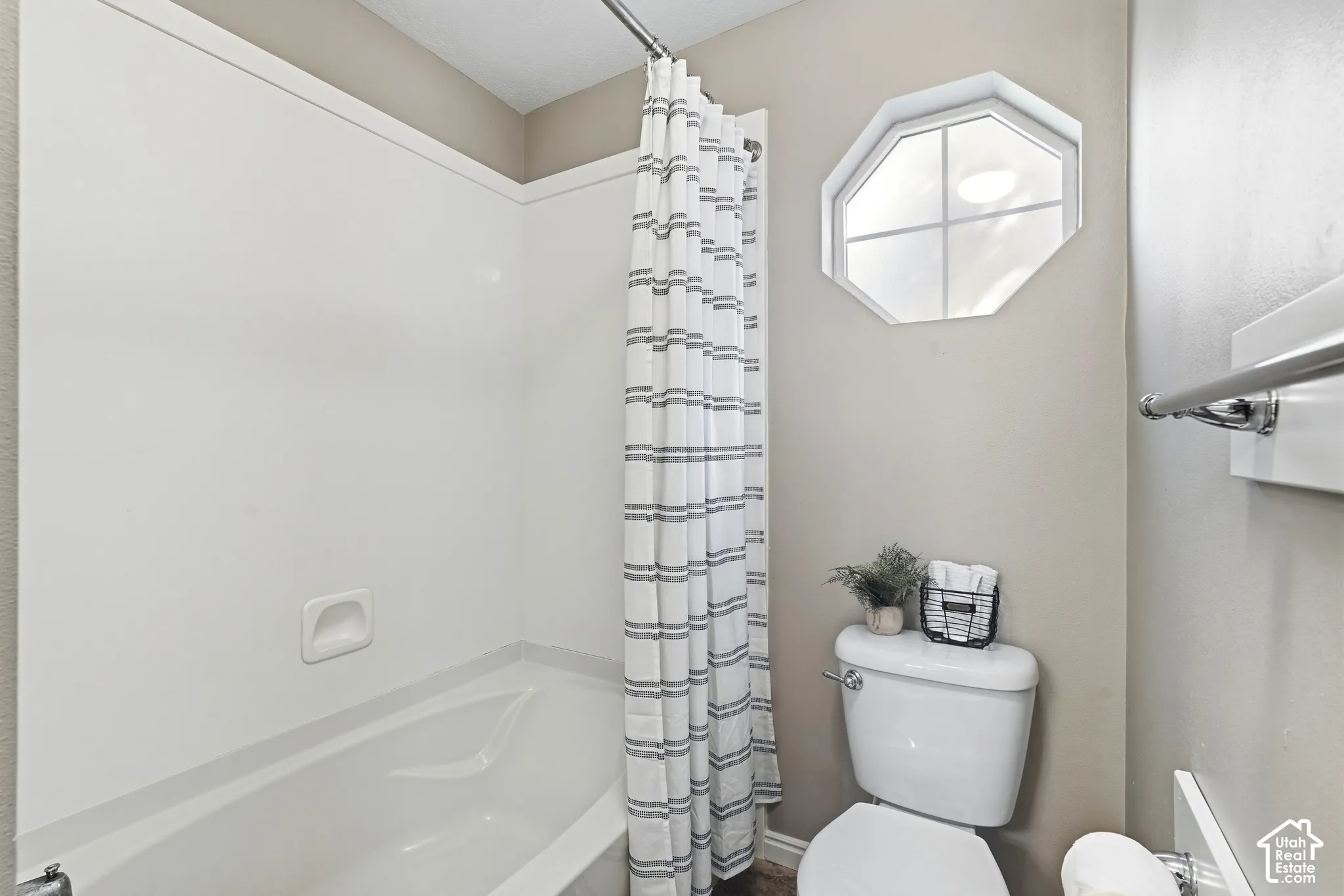 White bathtub with integrated shower, single-pane octagonal window, and chrome towel bar