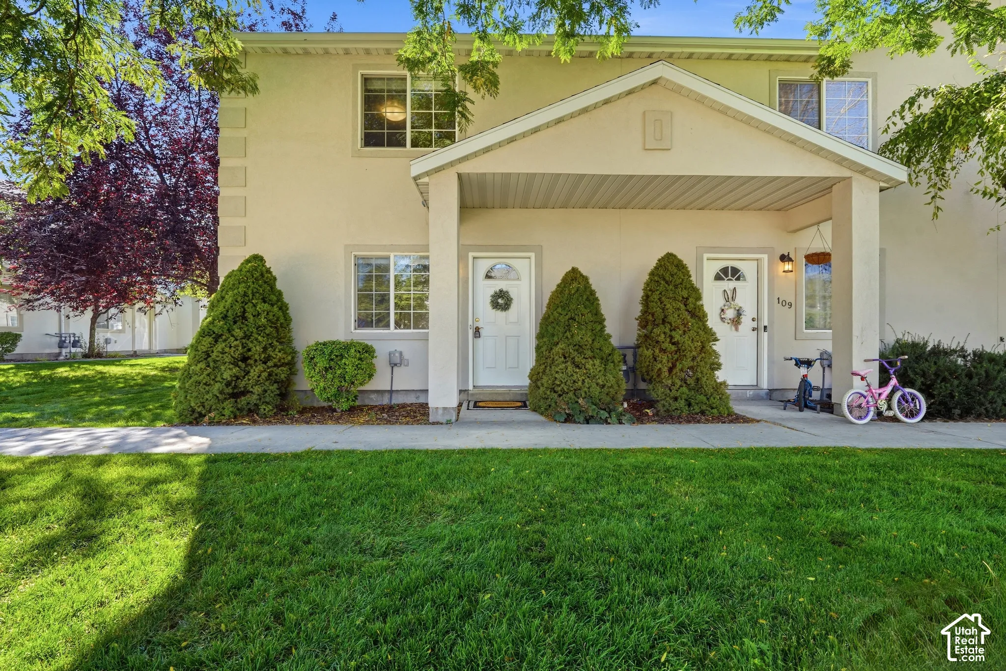 Stucco exterior with a covered porch entryway, featuring grid windows and a manicured lawn