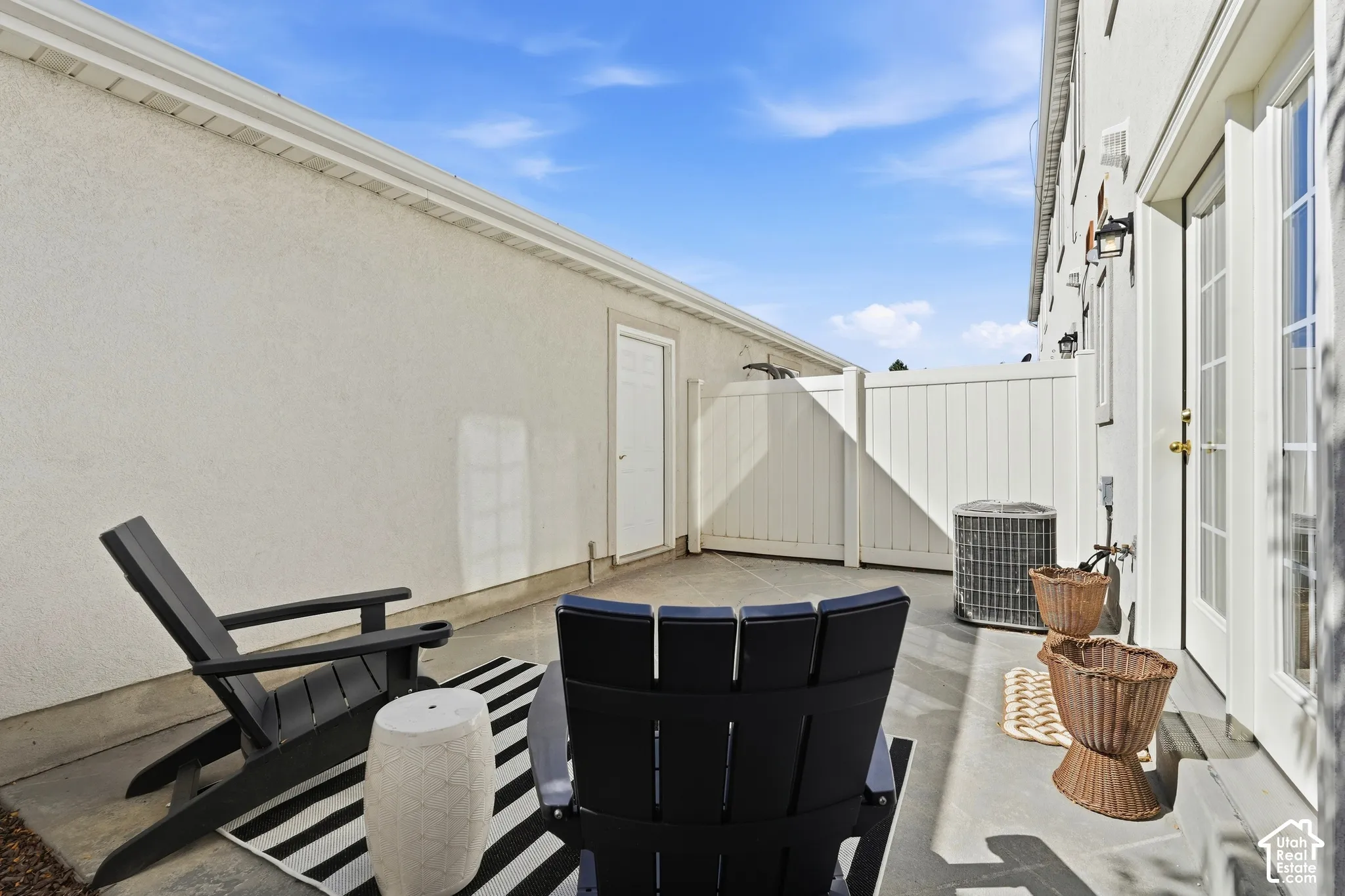 Private patio space featuring concrete flooring, a white privacy fence, and an exterior door with glass panels