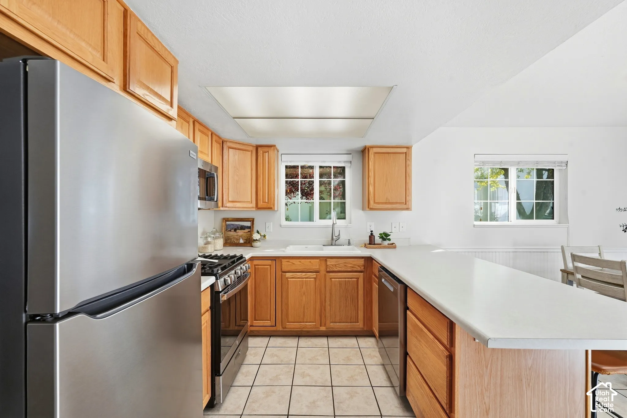 U-shaped kitchen with wood cabinetry, stainless steel appliances, white countertops, and tiled flooring
