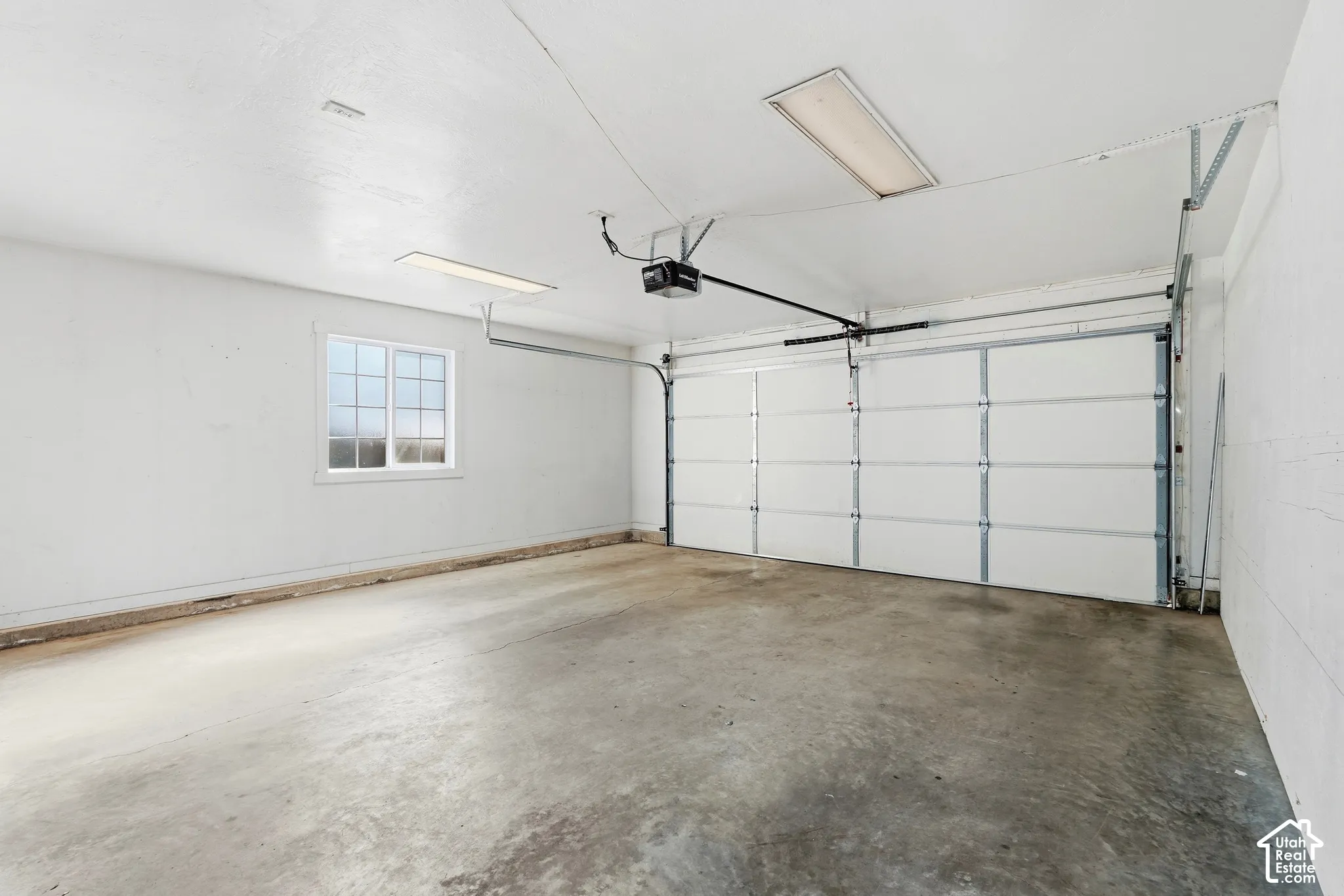 Two-car garage with concrete flooring, overhead fluorescent lighting, a paneled garage door, and a multi-pane window