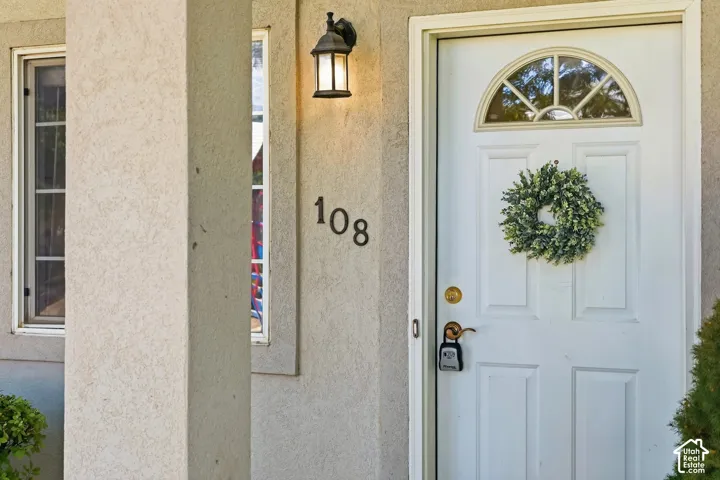Front entry featuring a white door with an arched transom window, a wall-mounted exterior light fixture, and textured stucco siding