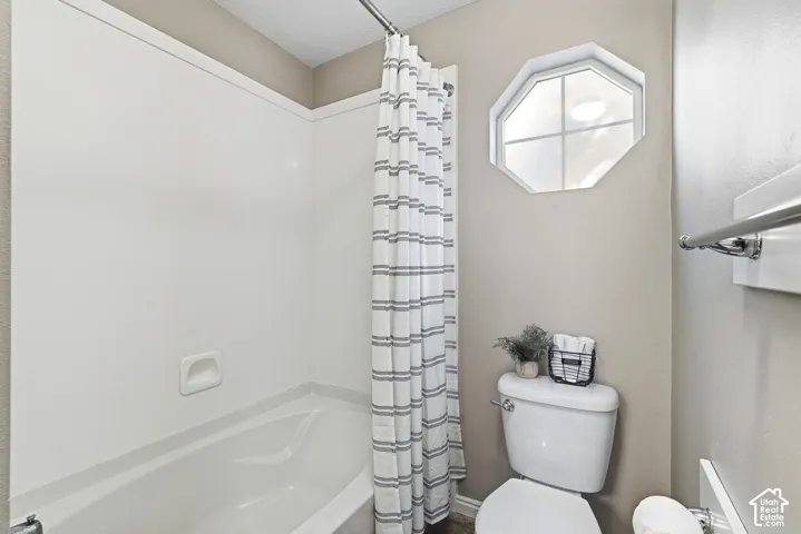White bathtub with integrated shower, single-pane octagonal window, and chrome towel bar