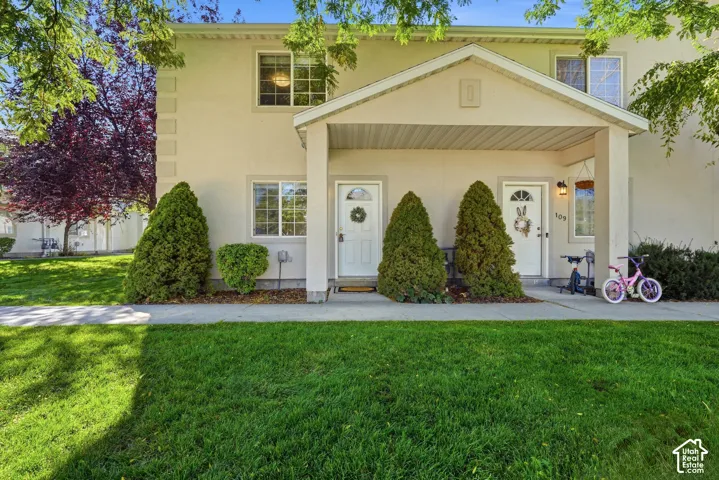 Stucco exterior with a covered porch entryway, featuring grid windows and a manicured lawn