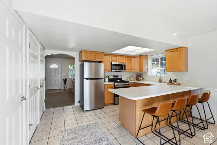 Kitchen featuring wood cabinetry, stainless steel appliances, a breakfast bar, and tile flooring