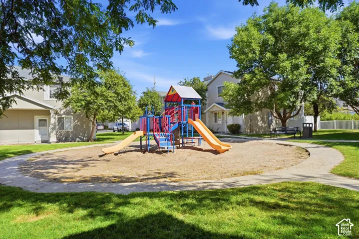 Community playground featuring slides and climbing structures, surrounded by a sand play area, manicured lawns, and mature trees