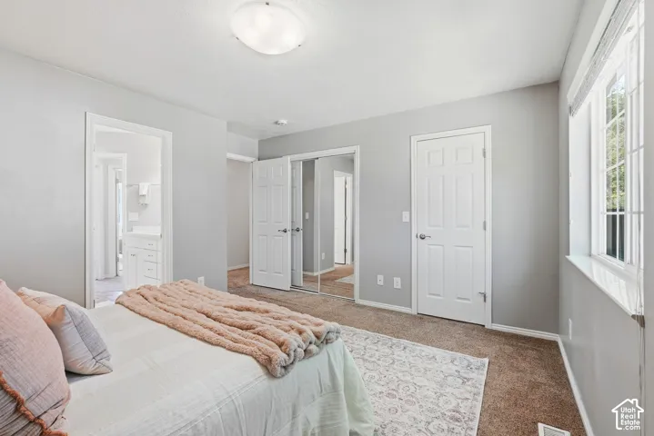 Carpeted bedroom featuring a large window, a paneled door, and a mirrored closet
