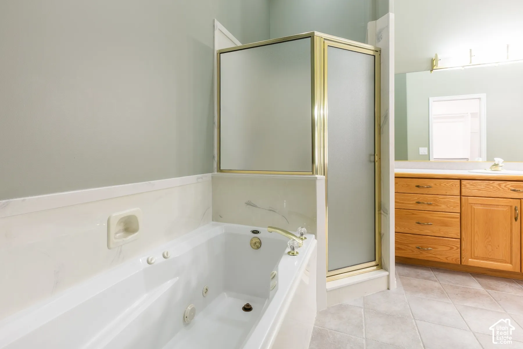 Jetted soaking tub with integrated soap niche, shower enclosure with brass-finish framing, wood cabinetry, and tile flooring