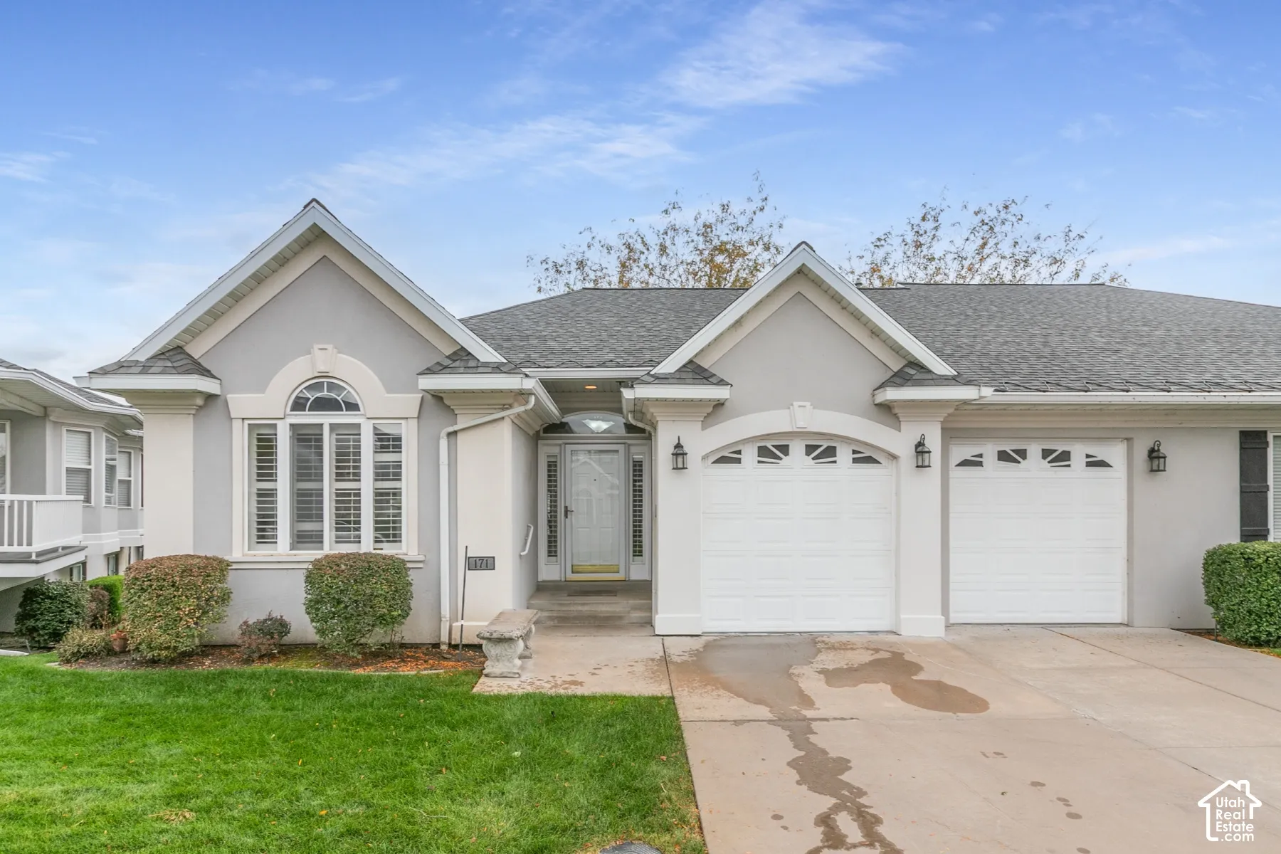 Stucco exterior featuring dual front-facing gables, arched window detailing, a two-car garage with paneled doors, and a concrete driveway