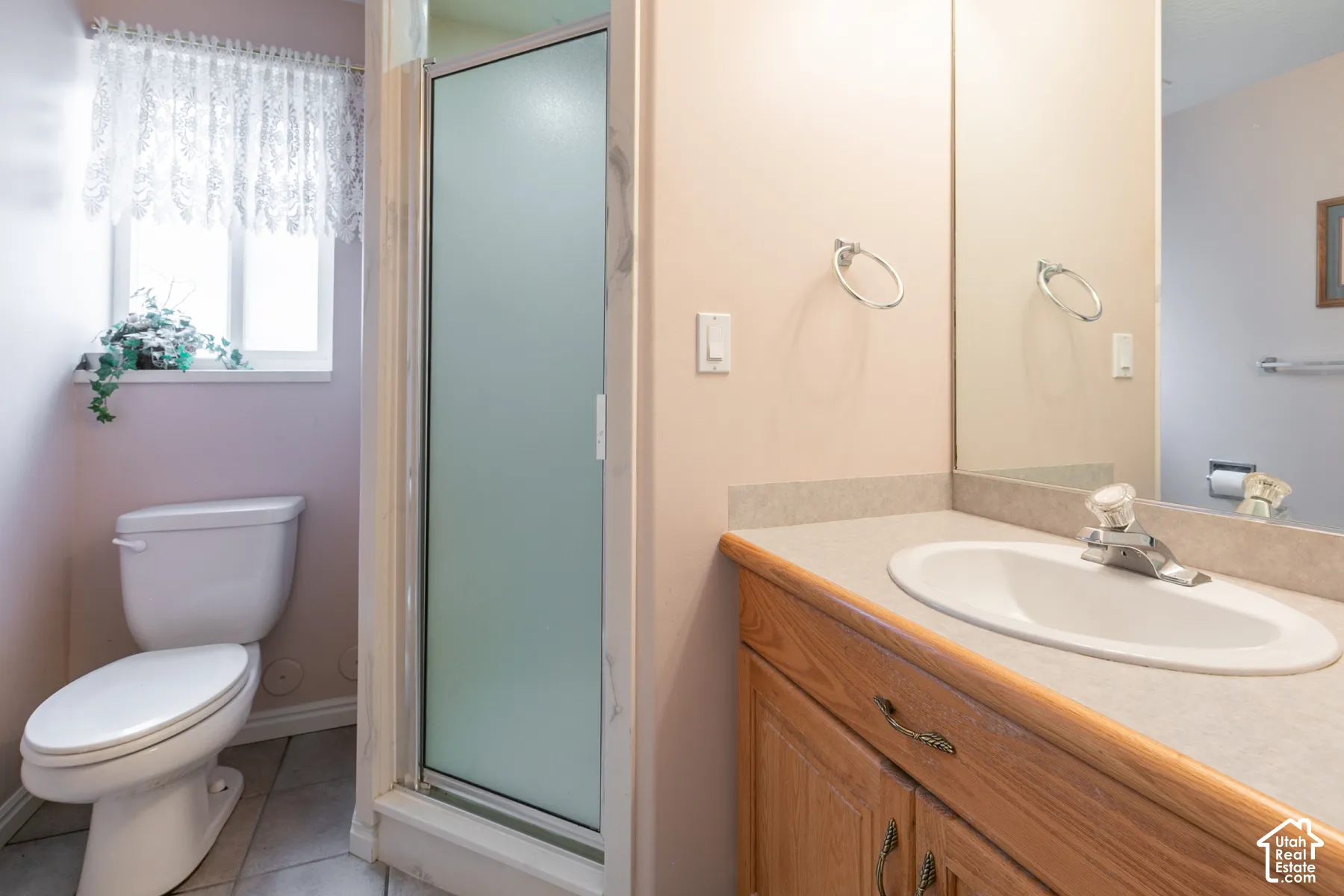 Bathroom featuring a wood-finish vanity with a solid-surface countertop and inset sink, tiled flooring, a shower stall with a frosted glass door, and a wall-mounted mirror