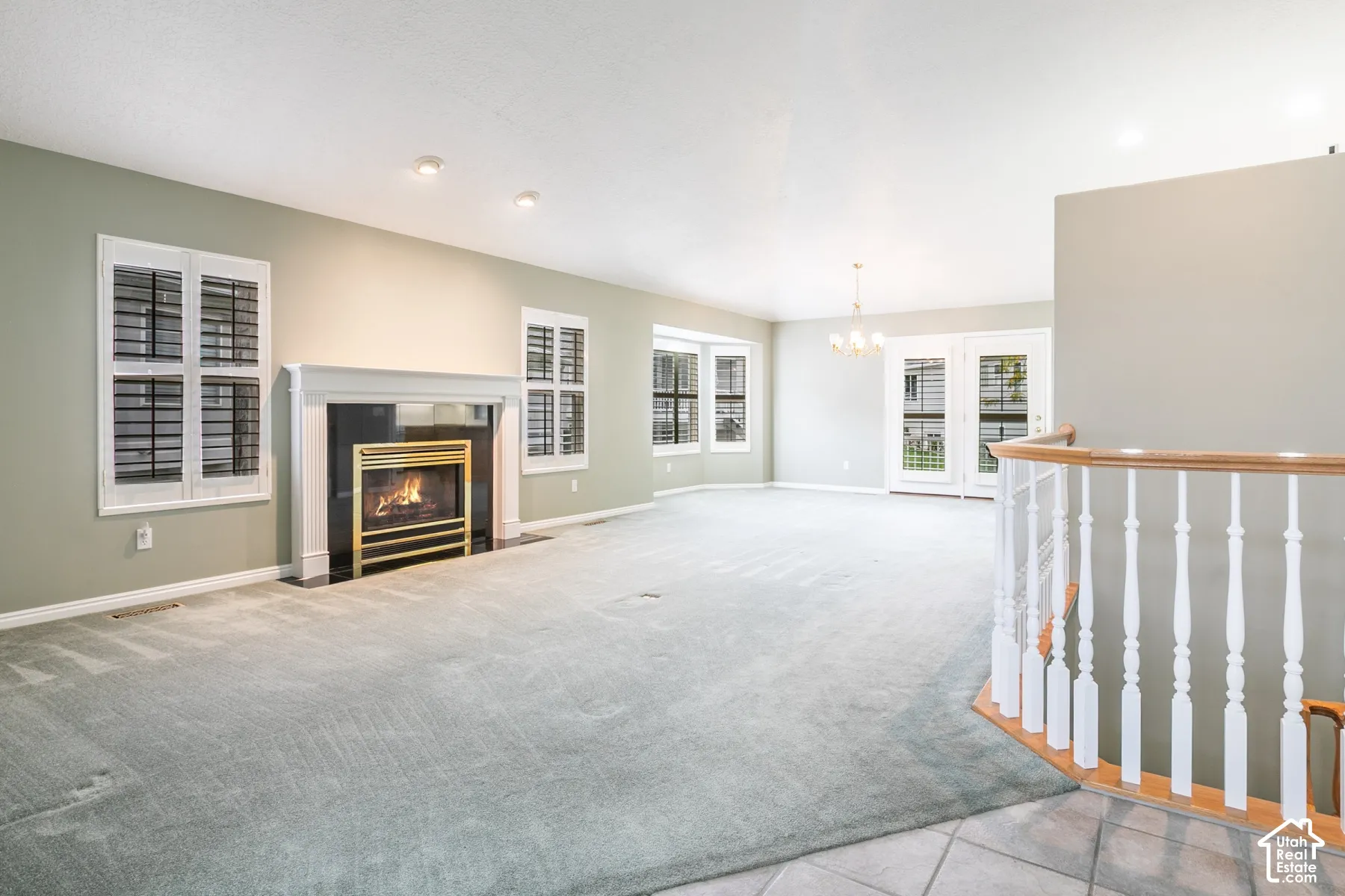 Gas fireplace with a decorative mantel, bay window, white-paned glass double doors, recessed lighting, and a white wood-railing staircase