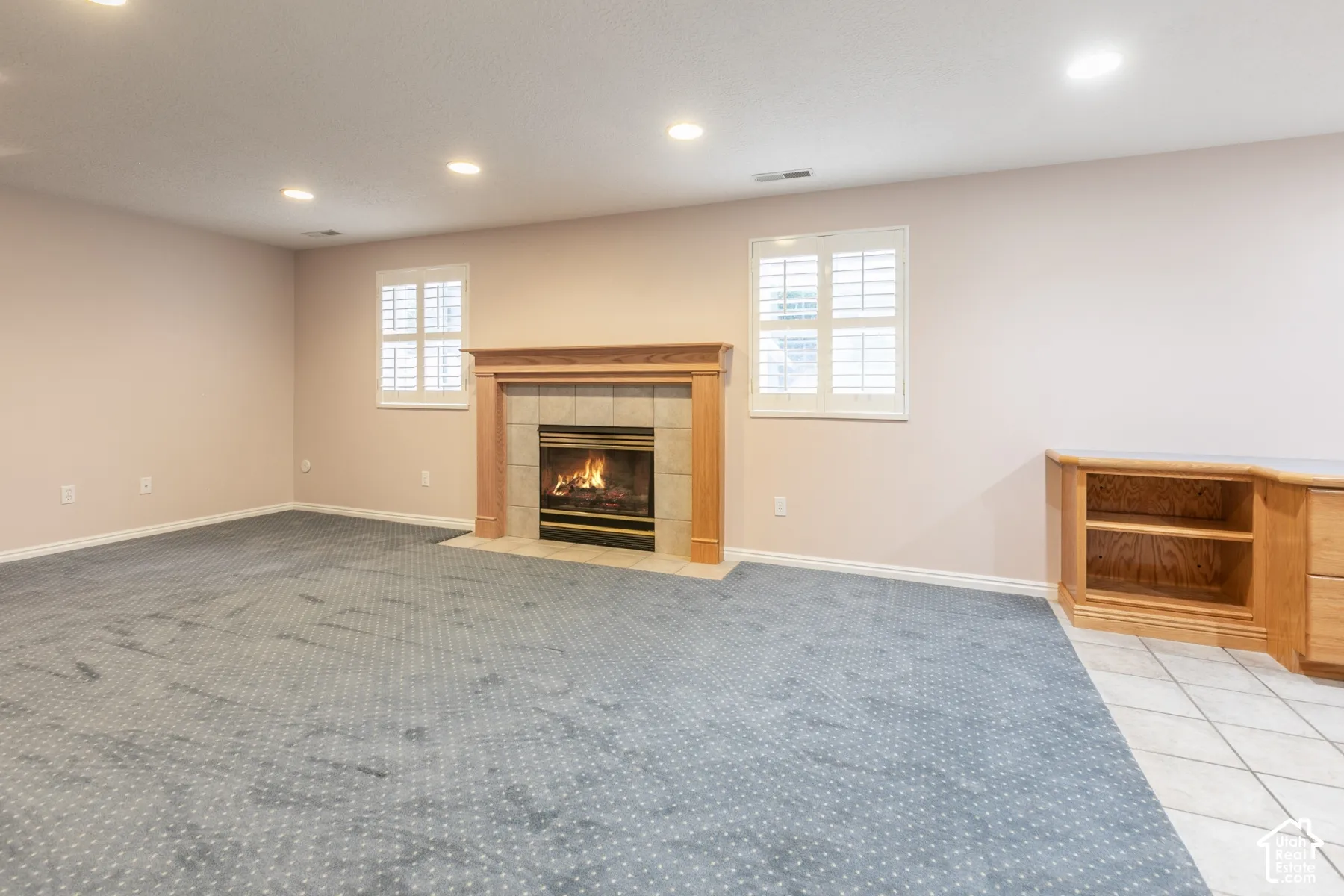 Fireplace with wood mantle and tile surround, recessed lighting, plantation shutters, and built-in wood cabinetry