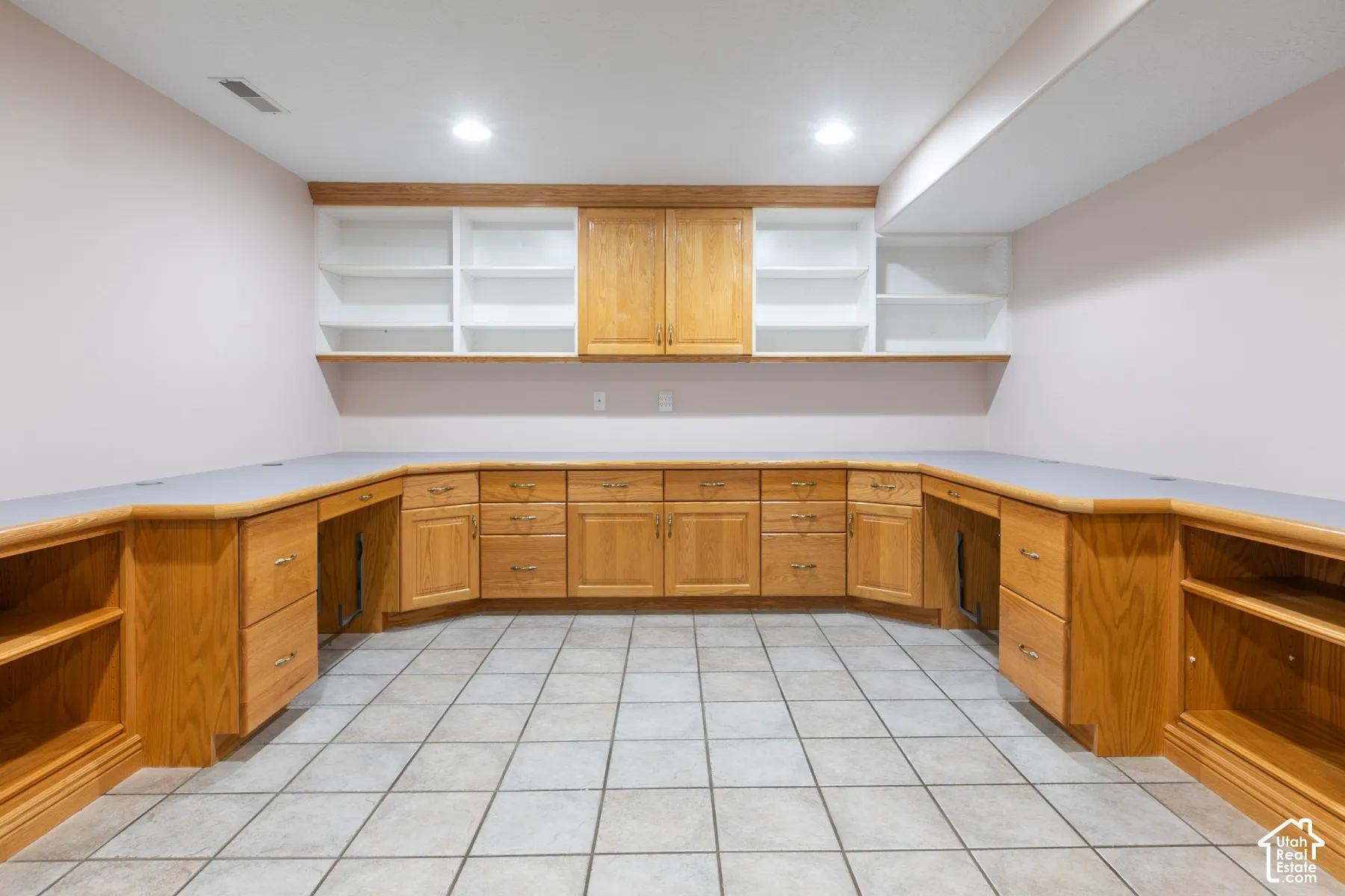 Custom built-in wood cabinetry, expansive continuous countertop workspace, overhead shelving units, recessed lighting, and ceramic tile flooring