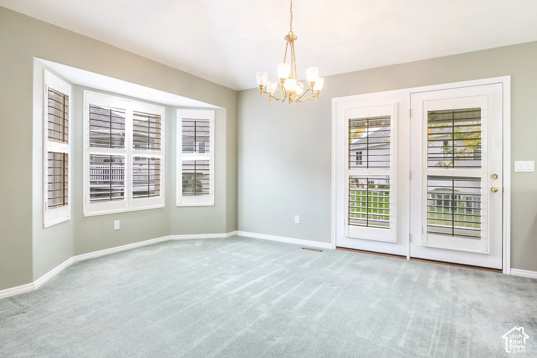 Bay window featuring plantation shutters, multi-light chandelier, and dual glass-paneled exterior doors with integrated shutter blinds