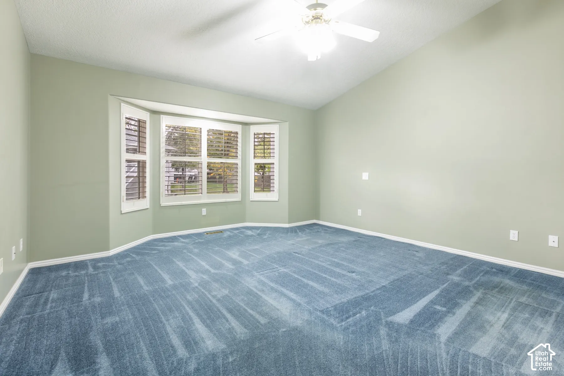 Vaulted ceiling with a central multi-blade ceiling fan, expansive bay window, and neutral wall tones