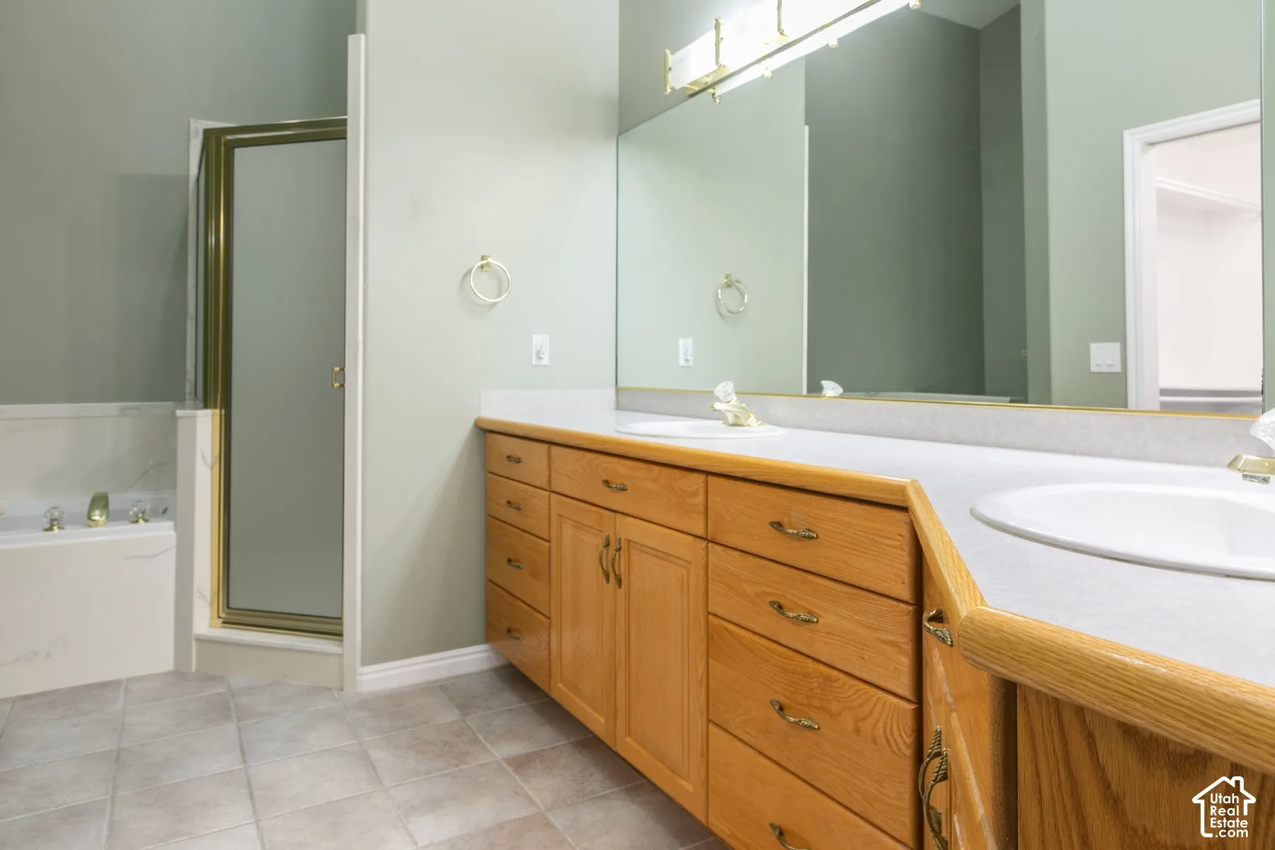 Dual-sink vanity with natural wood cabinetry, large vanity mirror, built-in soaking tub, and separate glass-enclosed shower