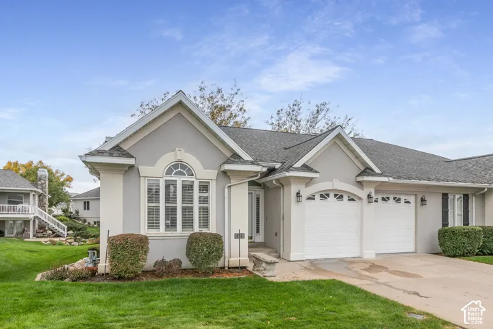 Single-story exterior featuring light gray stucco siding, contrasting white architectural trim, an arched window with decorative molding, a two-car garage, and a gabled roofline