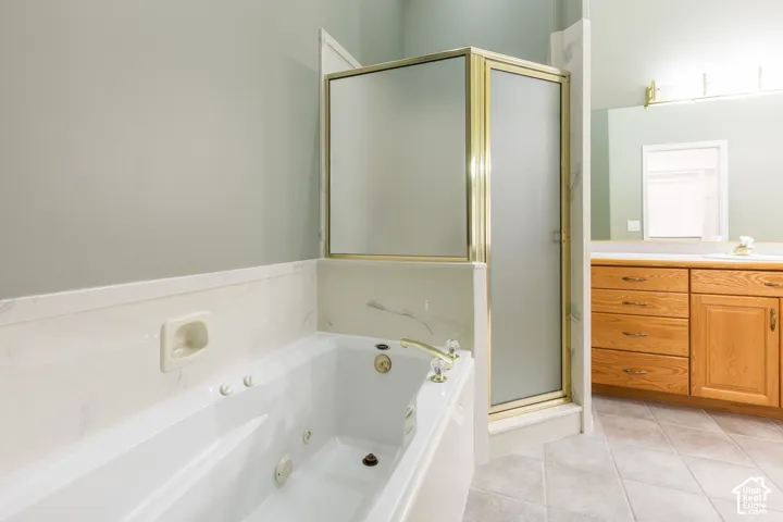 Jetted soaking tub with integrated soap niche, shower enclosure with brass-finish framing, wood cabinetry, and tile flooring