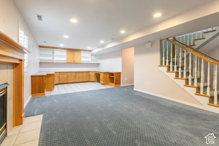 Wood-trimmed fireplace with tile hearth, recessed lighting, built-in wooden cabinetry, tile flooring, and a staircase with wooden handrail and balusters