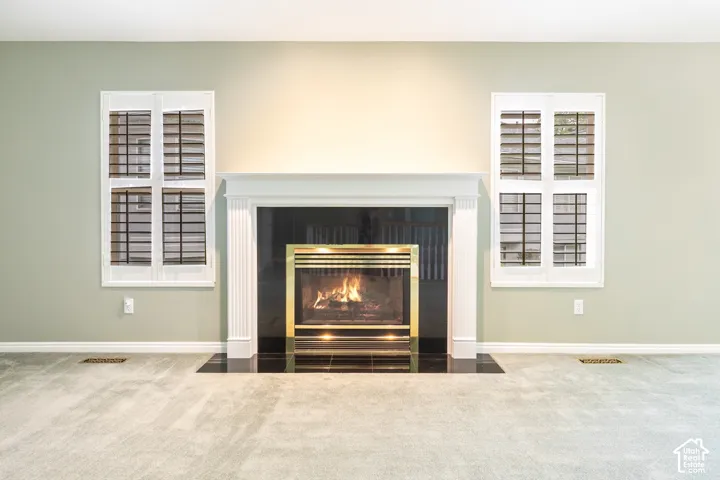 Fireplace featuring a fluted white mantel surround, black stone hearth, and metallic firebox trim, flanked by dual windows with white plantation shutters