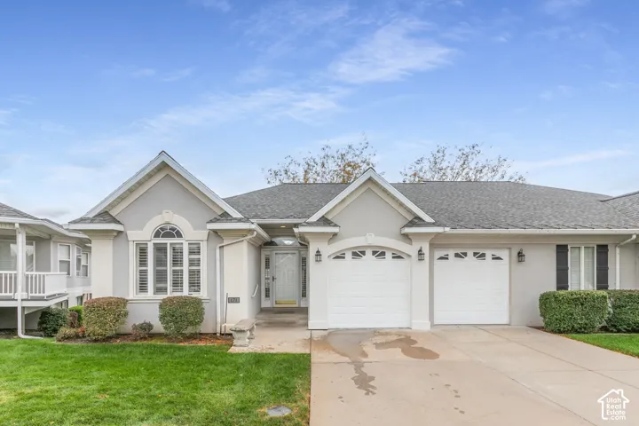Single-story residence featuring a gray stucco exterior, an arched entryway, double-pane windows with decorative trim, an attached two-car garage, and manicured landscaping