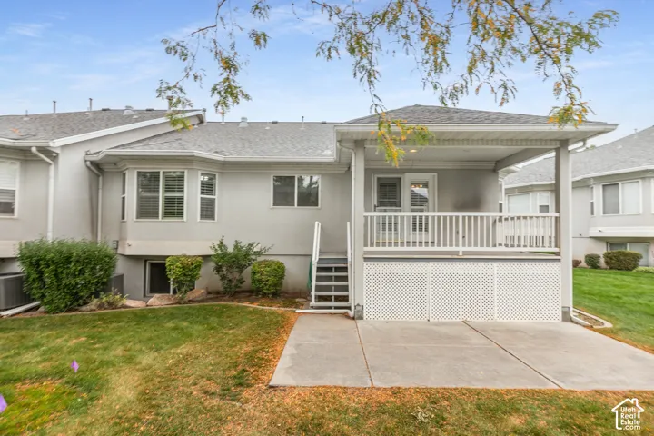 Rear exterior featuring a covered deck with white railing, lattice skirting, concrete patio, and a bay window