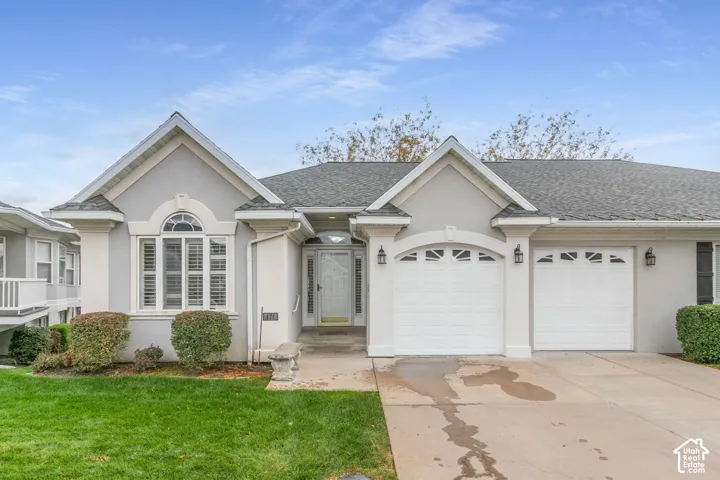 Stucco exterior featuring dual front-facing gables, arched window detailing, a two-car garage with paneled doors, and a concrete driveway