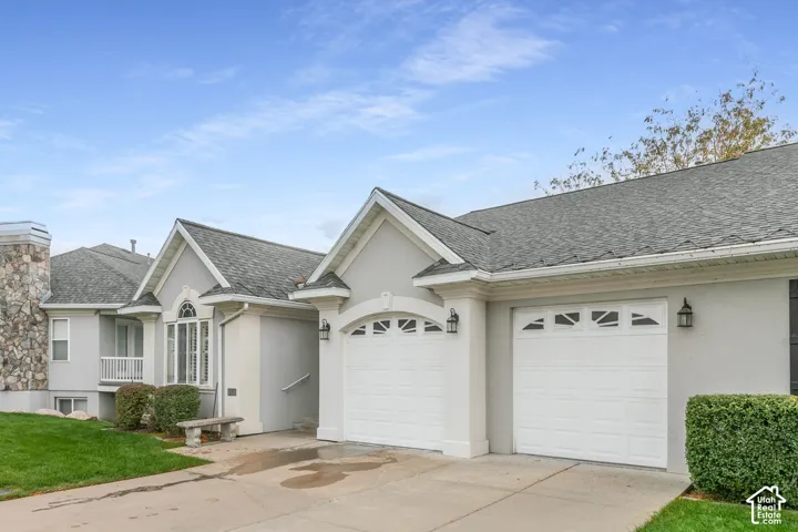 Exterior elevation featuring a light-toned stucco facade, dual-bay garage with decorative window detailing, arched architectural accents, and shingle roofing