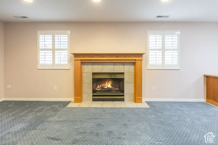 Fireplace with a wood-finish mantel and stone-tile surround, dual windows with plantation shutters, recessed ceiling lighting, and wall-to-wall carpeting
