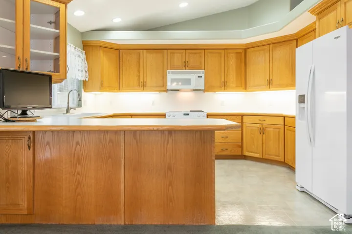 Kitchen featuring extensive oak cabinetry, a peninsula island, vaulted ceilings, recessed lighting, and integrated appliance placement