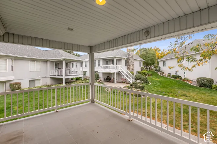 Covered balcony featuring tile flooring and white metal railing overlooking a common green space with mature landscaping