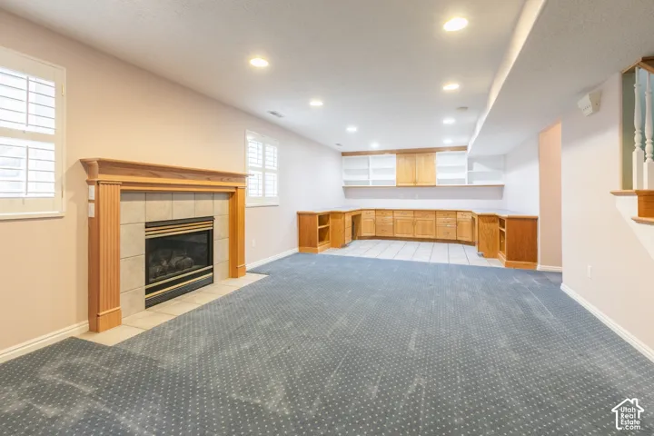Fireplace with wood mantel and tiled surround, custom wood-finish built-in cabinetry, recessed lighting, and plantation shutters