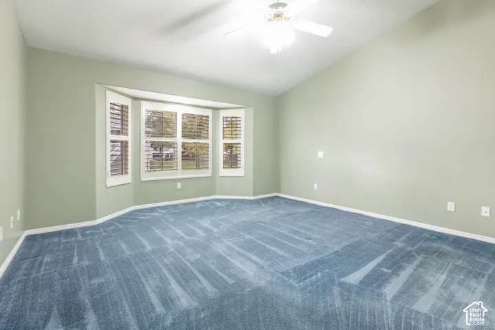 Vaulted ceiling with a central multi-blade ceiling fan, expansive bay window, and neutral wall tones