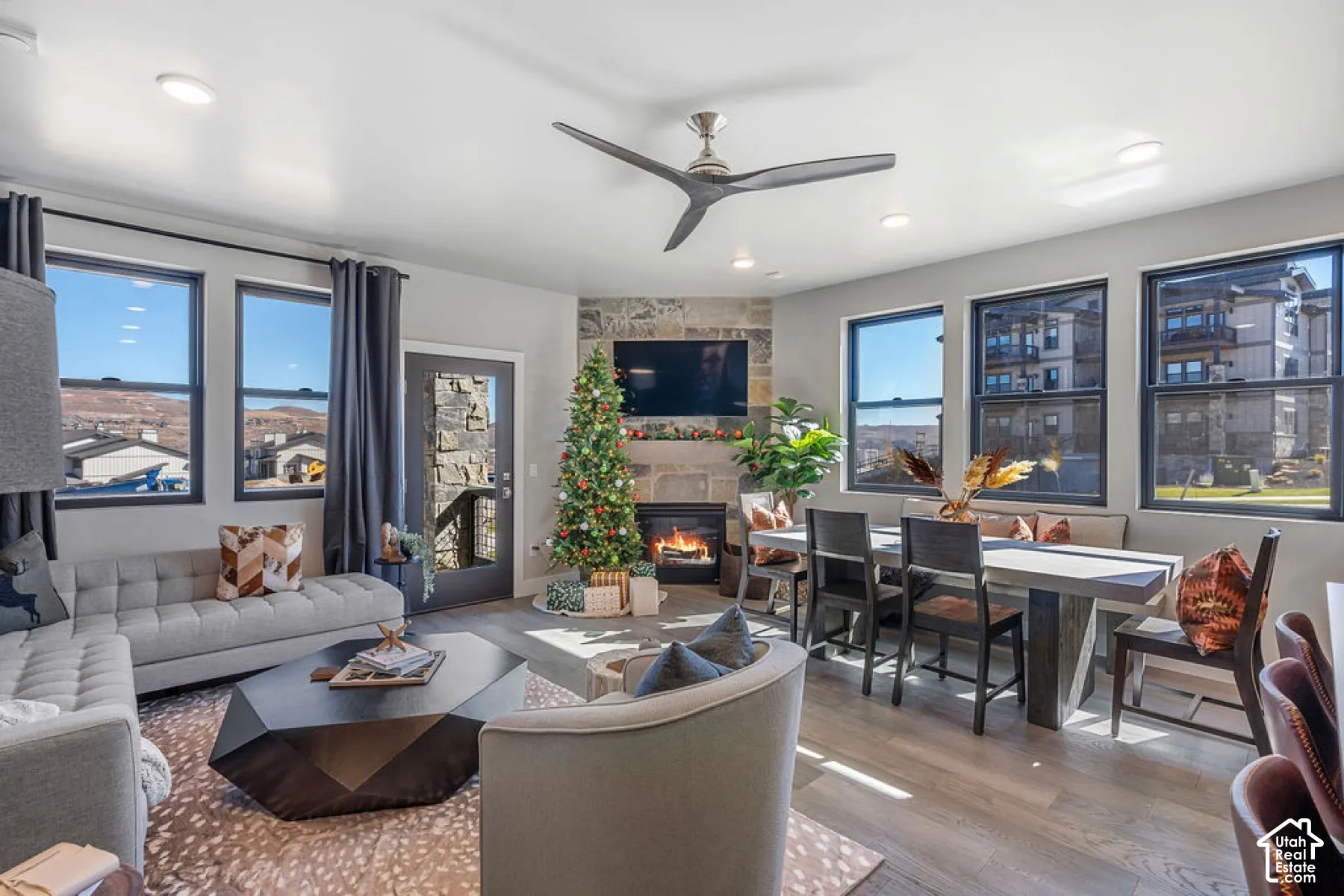 Open-concept living space with wood-finish flooring, a stone-clad fireplace, and multiple windows
