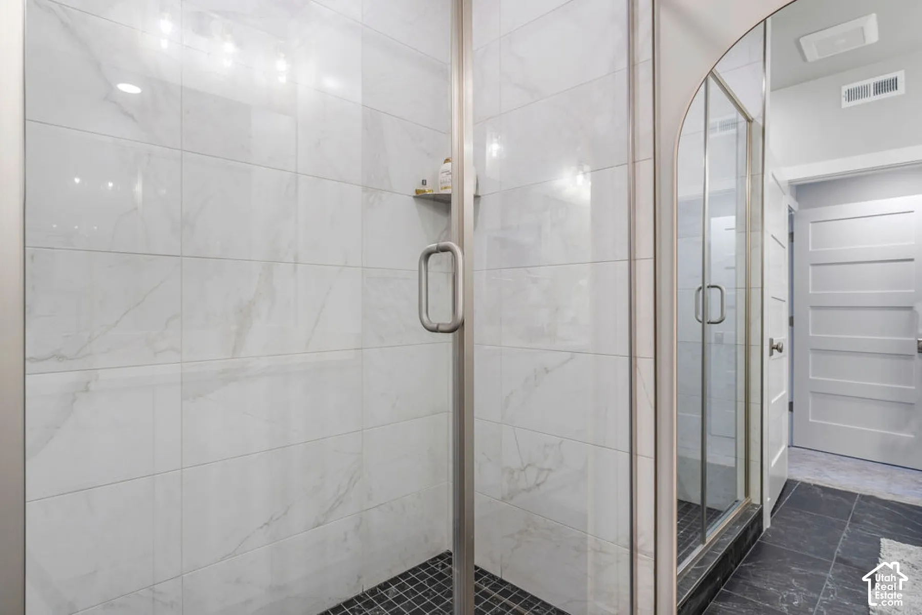 Glass-enclosed shower with large format white tile walls, a built-in shower niche, and a black mosaic tile floor