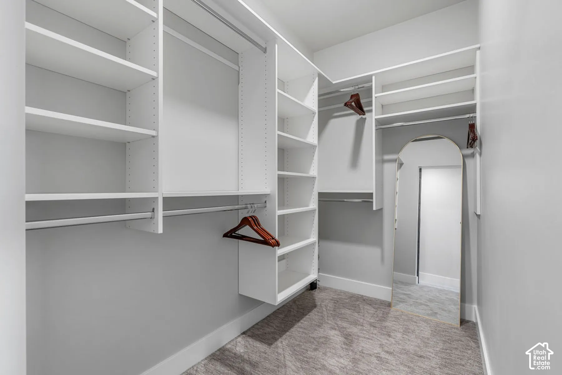 Custom closet system featuring multiple shelving units and hanging rods, light gray wall paint, and gray patterned carpet flooring
