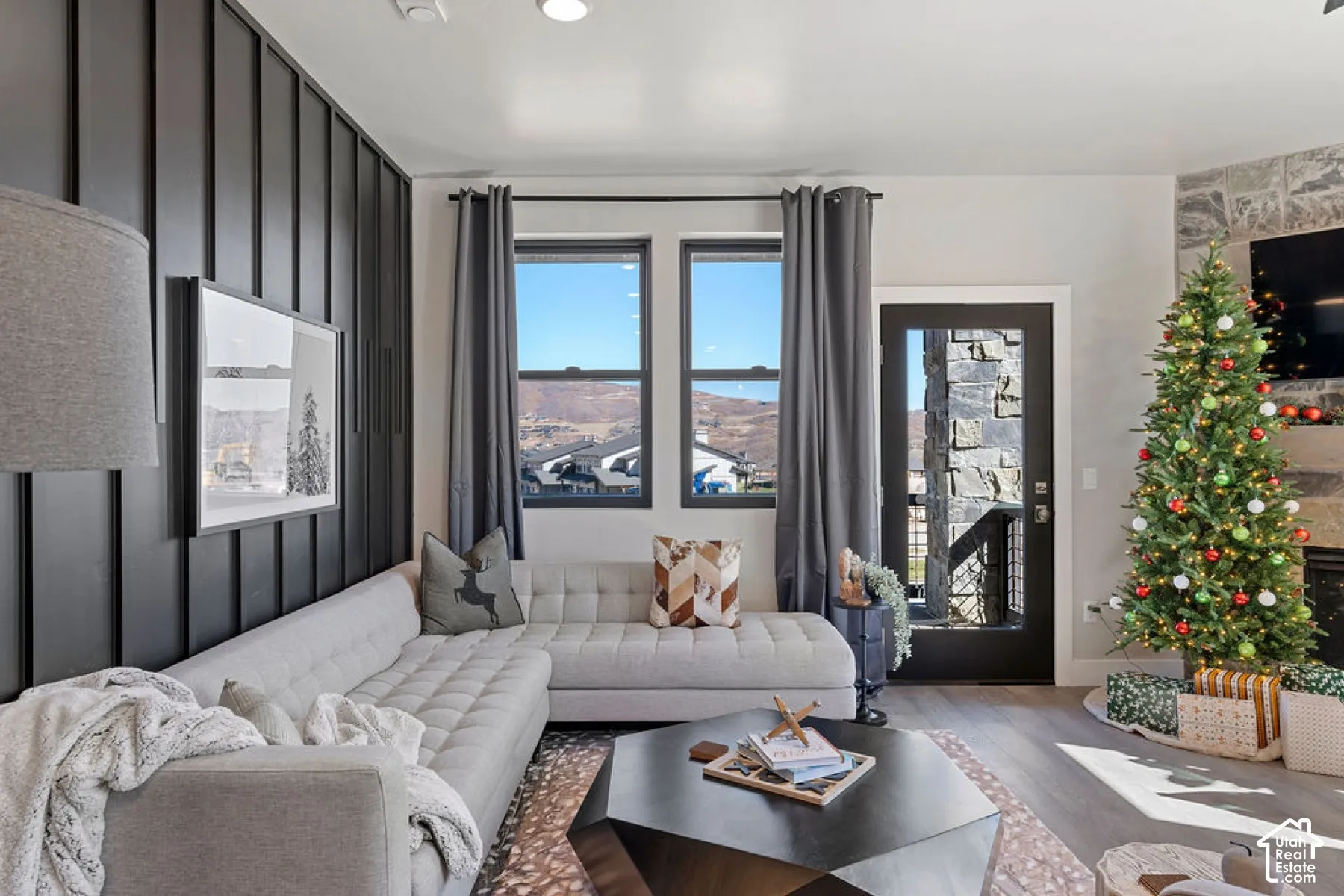 Board and batten accent wall, wood-finish flooring, stone-clad fireplace, large windows, and a glass-paneled door