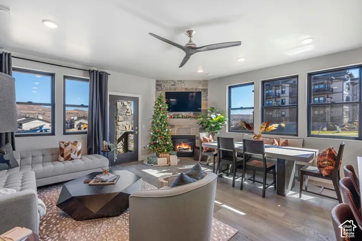 Open-concept living space with wood-finish flooring, a stone-clad fireplace, and multiple windows