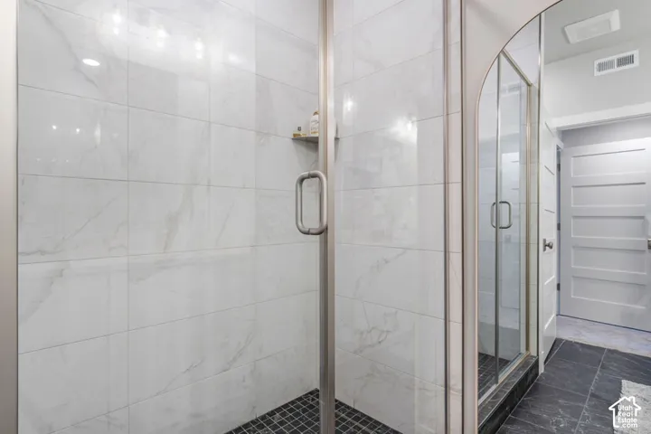 Glass-enclosed shower with large format white tile walls, a built-in shower niche, and a black mosaic tile floor